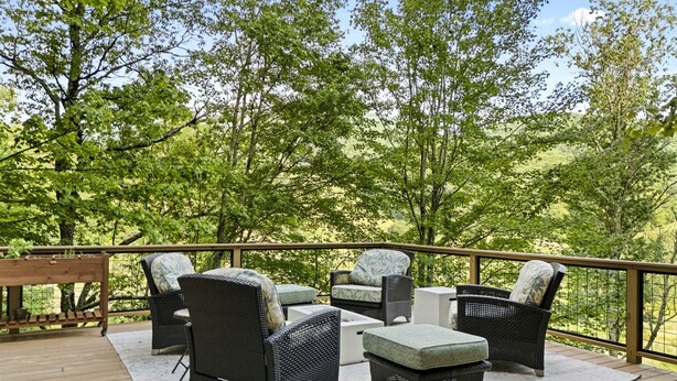 A deck with wicker furniture, a wooden table, and a white rug.