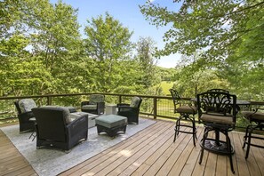 A wooden deck with outdoor furniture, including chairs and a table, overlooking a lush green landscape.