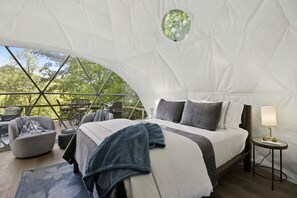 A tent-style room with a bed, a chair, a table, and a lamp.
