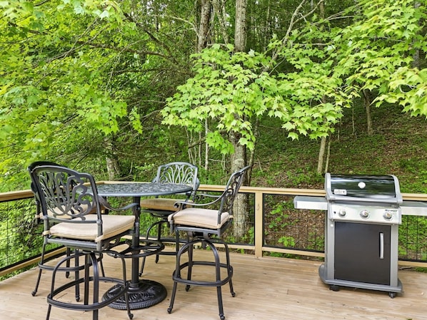 Eine Terrasse im Freien mit Tisch, Stühlen, einem Grill und einem Holzgeländer.