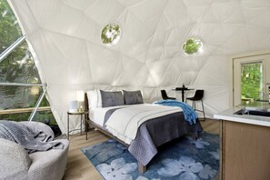 Alojamiento en tienda de campaña con cama, mesita de noche, lámpara, sillas y una pequeña cocina.