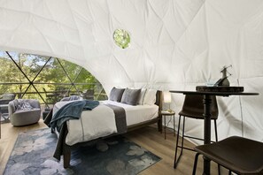 Alojamiento en tienda de campaña con cama, zona de estar, mesa y vistas al exterior.