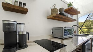 A modern kitchen with a Keurig coffee maker, an induction cooktop, a toaster oven, and wooden shelves with kitchen items.