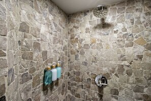 A stone-walled shower with a handheld showerhead and a wall-mounted faucet.