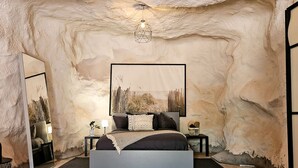 Quarto com uma cama grande, um quadro na parede, uma mesa de cabeceira com abajur e um espelho na parede à esquerda.