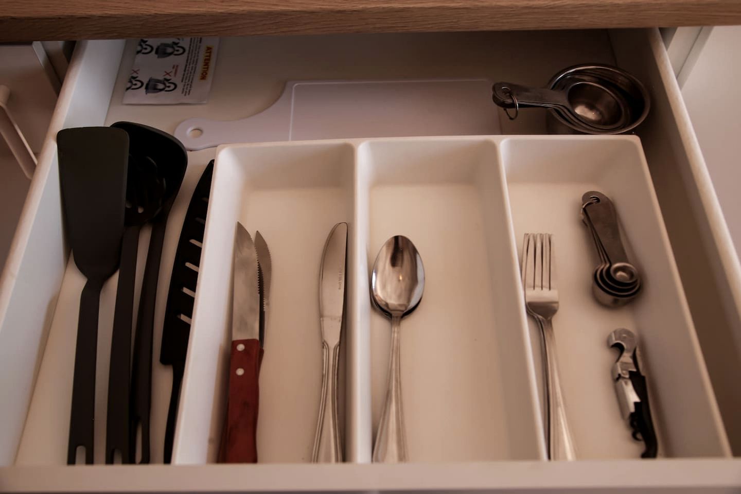 Un tiroir contenant des ustensiles rangés avec soin, notamment des couteaux, une cuillère, une fourchette et un ouvre-boîte.