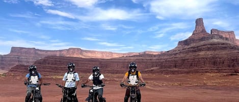 Three people on motorcycles in a desert landscape with red rock formations.