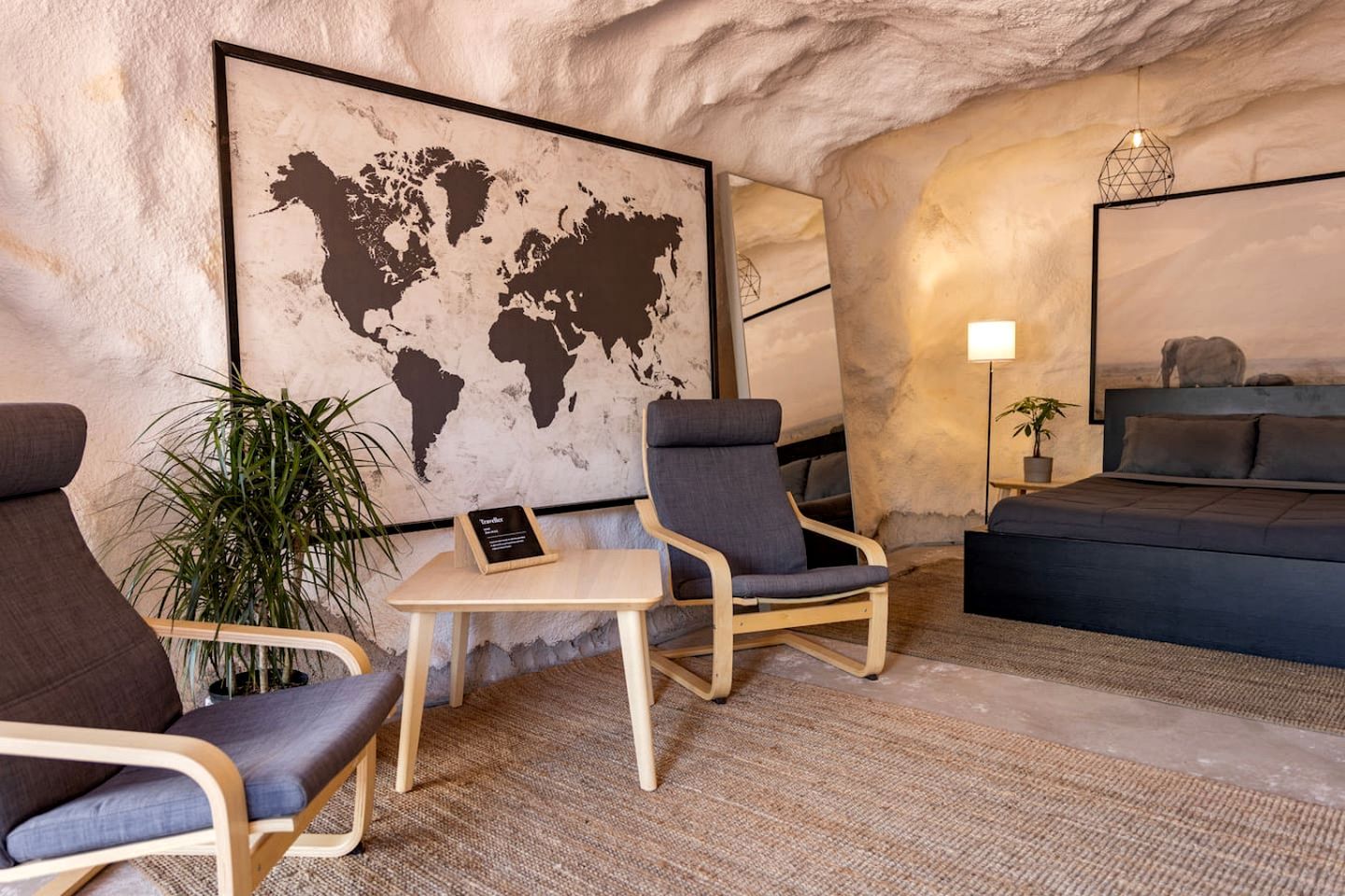 Una habitación con un mapa mundial, dos sillones, una mesita, una cama y una lámpara.