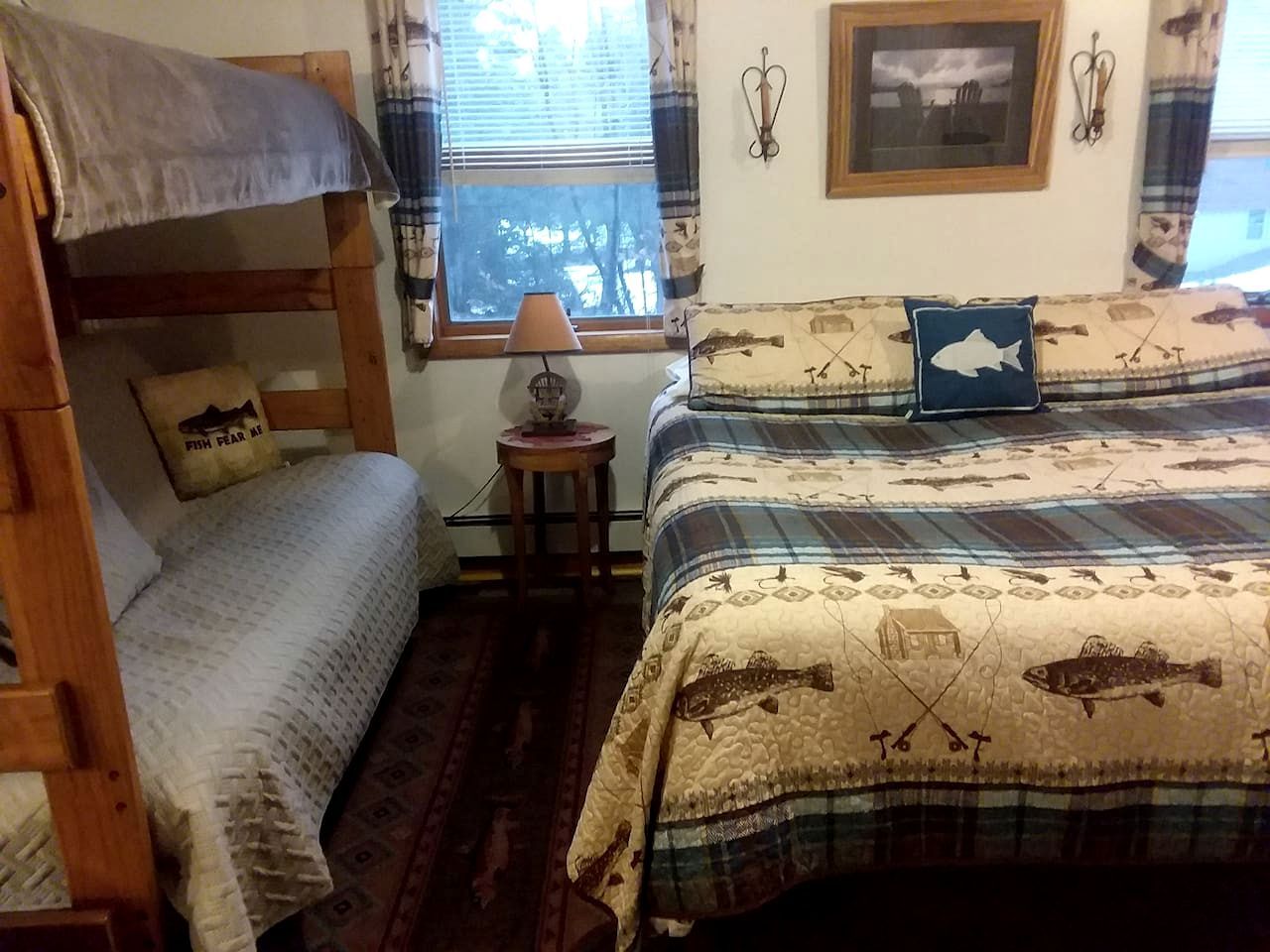 Una habitación con literas, una mesita con lámpara y una ventana con cortinas.