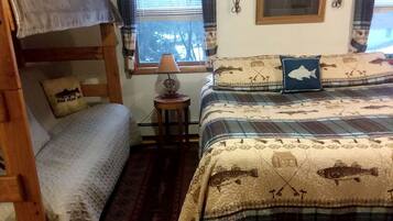 Una habitación con literas, una mesita con lámpara y una ventana con cortinas.