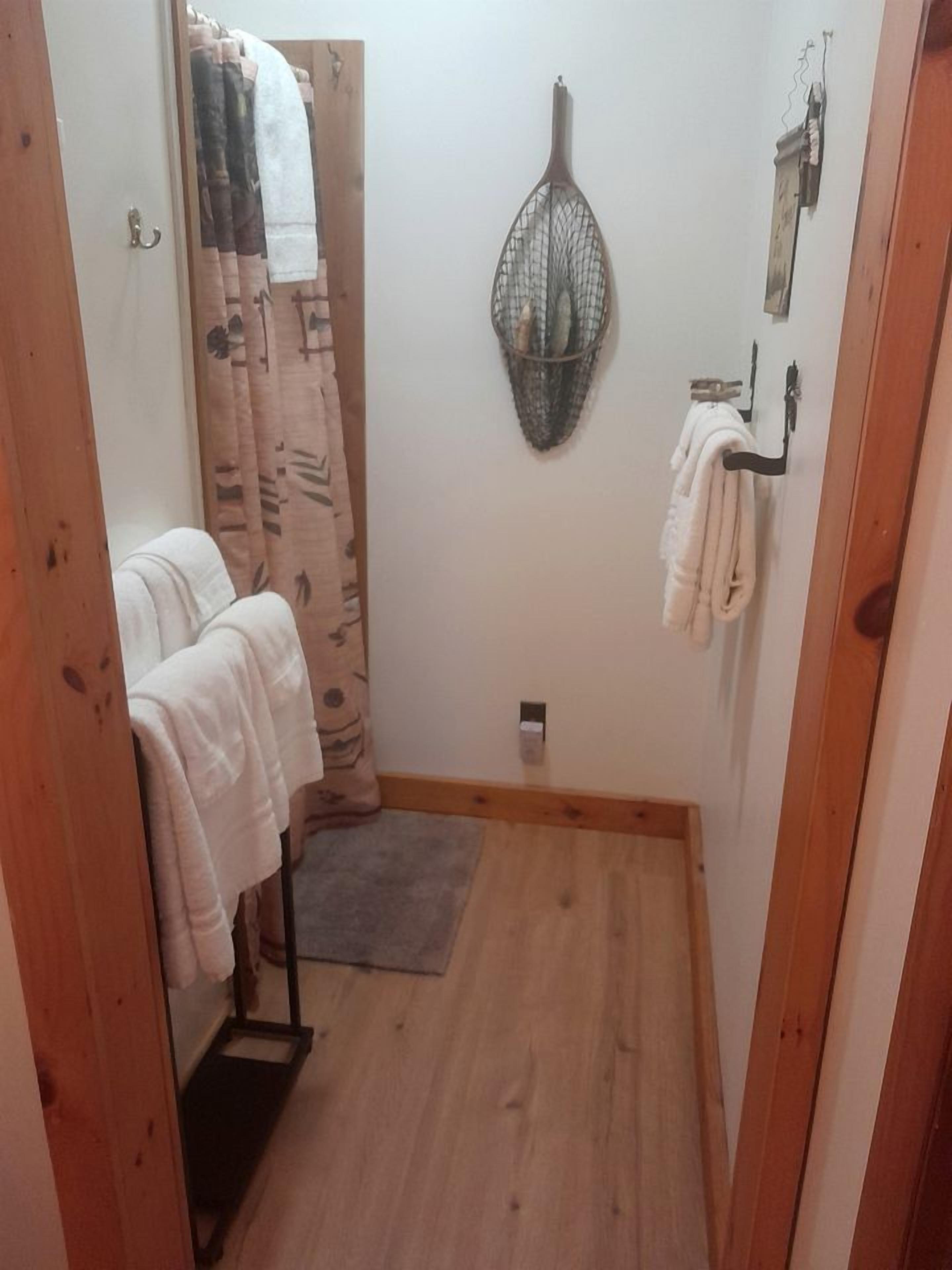 Une petite salle de bain avec un plancher en bois, un porte-serviettes, un rideau de douche et un autre porte-serviettes fixé au mur.