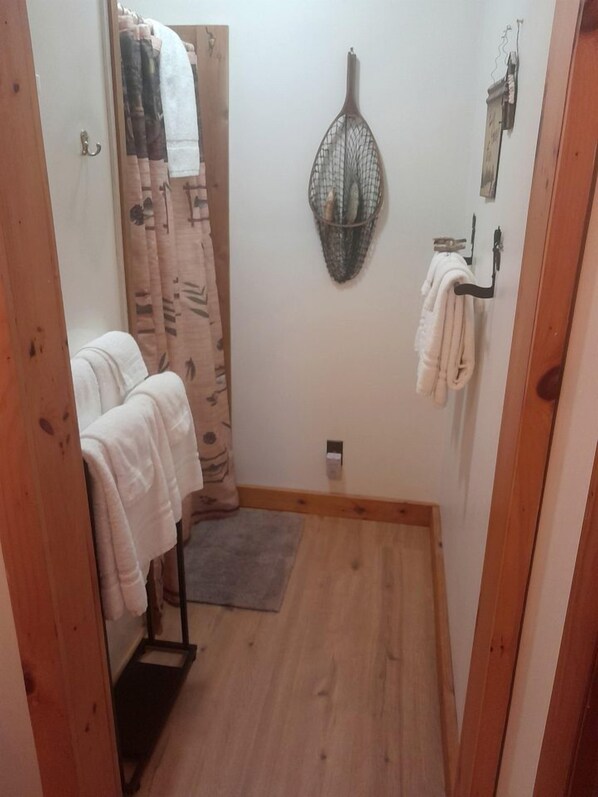 A small bathroom with a wooden floor, a towel rack, a shower curtain, and a wall-mounted towel rack.