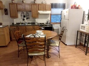 A kitchen with wooden cabinets, a stove, a refrigerator, and a dining table with chairs.