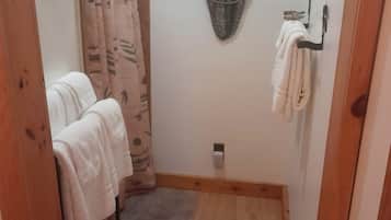 Un baño pequeño con suelo de madera, un perchero, una cortina de ducha y un toallero de pared.