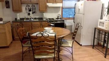 A kitchen with wooden cabinets, a stove, a refrigerator, and a dining table with chairs.