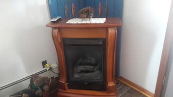 Una chimenea en esquina con un muro azul decorativo al fondo, una alfombra de pie y una pequeña alfombra en el suelo.