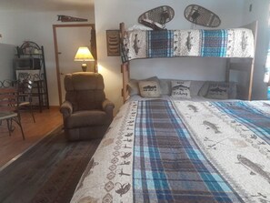Ein Stockbett mit gemustertem Bettbezug, ein Stuhl, eine Lampe und ein an der Wand befestigtes Regal.