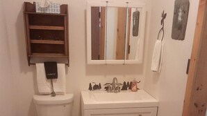 Een compacte badkamer met toilet, wastafel en een klein schapje boven het toilet.