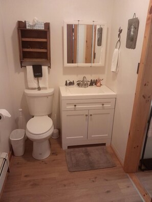 Un baño pequeño con inodoro, lavamanos y un estante sobre el inodoro.