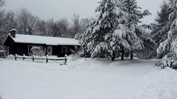 A snow-covered landscape with a house, trees, and a fence.