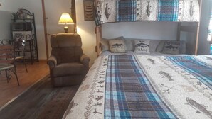Een stapelbed met een bedsprei met dessin, een stoel, een lamp en een wandplank.