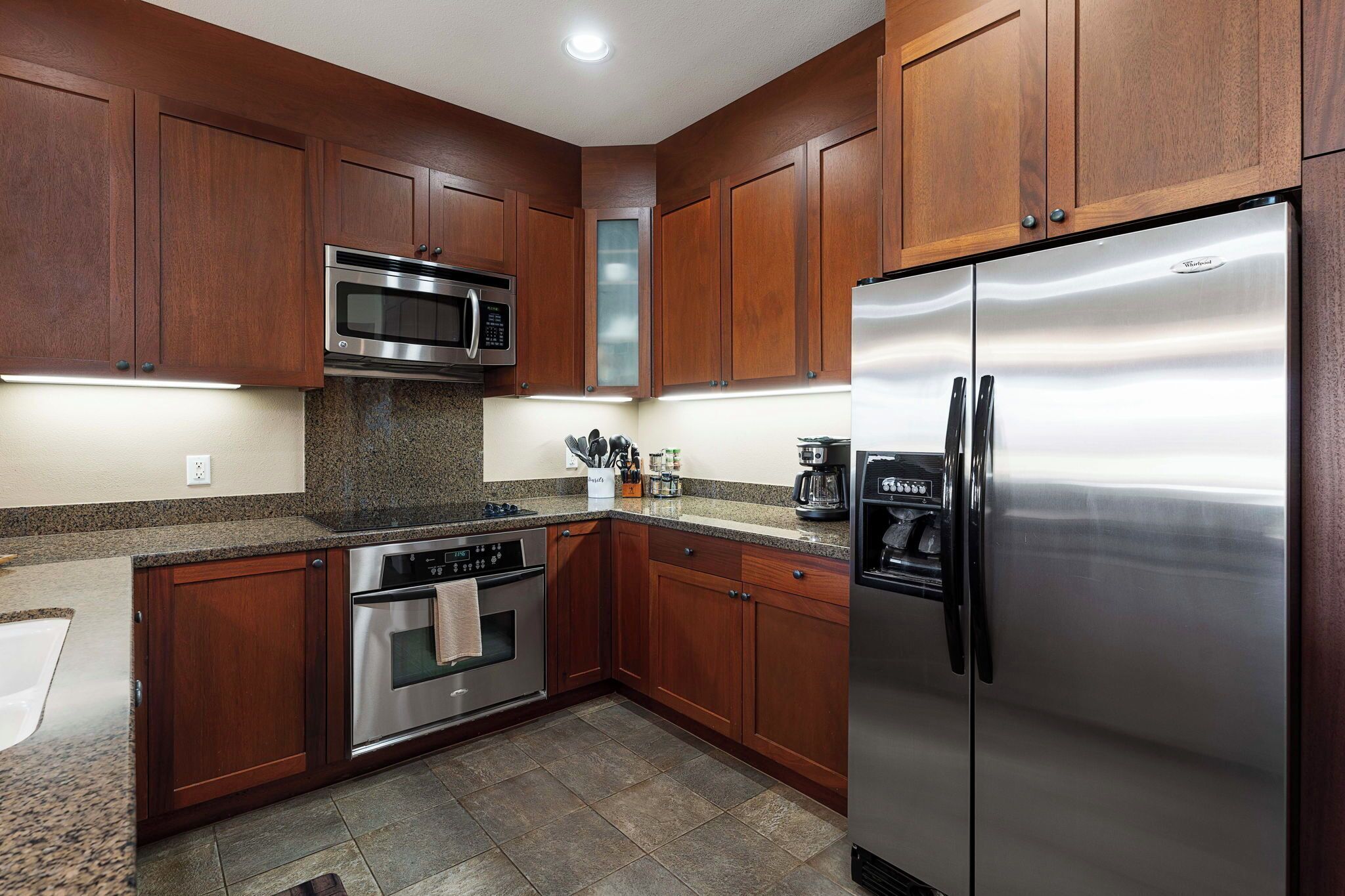 A kitchen with wooden cabinets, stainless steel appliances, granite countertops, and a built-in oven.