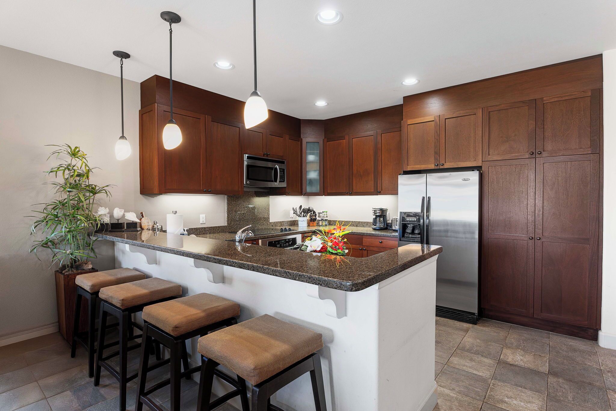 A modern kitchen with dark wood cabinets, stainless steel appliances, a granite countertop, and bar stools.