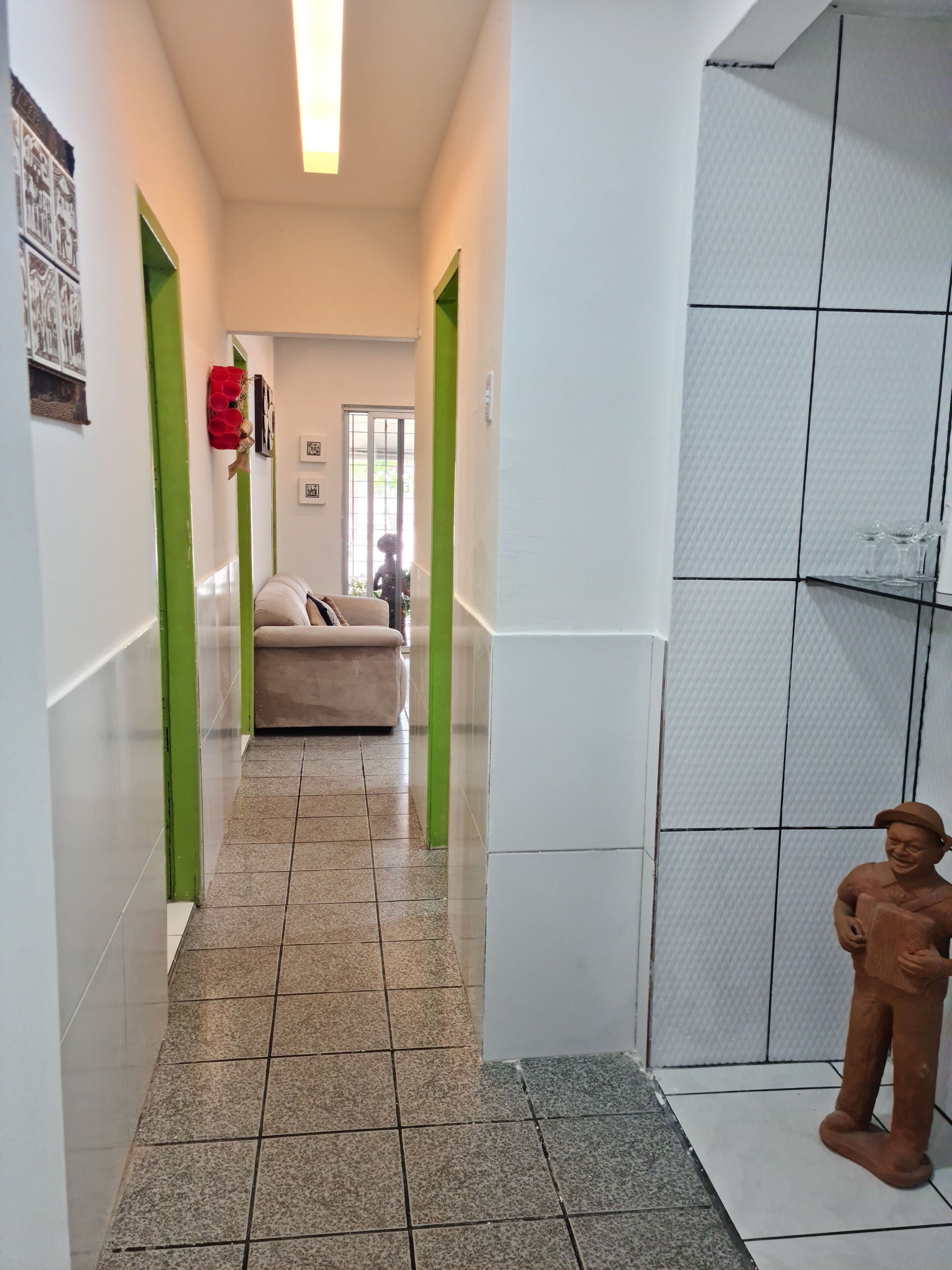 Un couloir doté d’un sol carrelé, de murs d’un vert vif, d’un canapé beige et d’une statue.