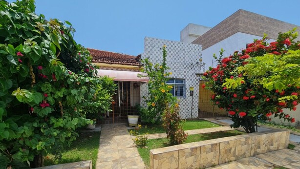 A courtyard with a tiled pathway, a small garden, and a building with a tiled roof and white walls. - Welcome to Casa Trajano in Olinda! Here, you will find comfort! (Olinda)