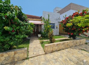 A courtyard with a tiled pathway, a small garden, and a building with a tiled roof and white walls. - Welcome to Casa Trajano in Olinda! Here, you will find comfort! (Olinda)