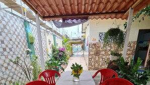 A covered patio with a table and red chairs, surrounded by potted plants and a tiled wall. - Welcome to Casa Trajano in Olinda! Here, you will find comfort! (Olinda)