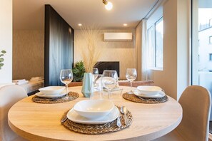 A round dining table set with white plates, bowls, and wine glasses, with a modern interior design and a view of the outside. - Porto Gallery District: Escape | A Central Haven (Porto)