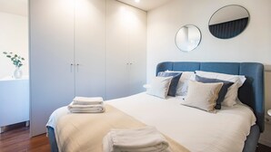 Ein modernes Schlafzimmer mit einem ordentlich bezogenen Bett, einem großen Kleiderschrank und zwei Wandspiegeln.