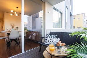 A modern living space with a dining area, a seating area with a sofa and cushions, and a round table with breakfast items. - Porto Gallery District: Escape | A Central Haven (Porto)
