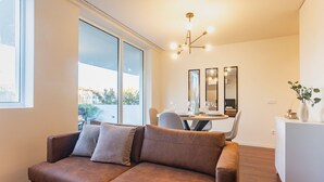 Ein modernes Wohnzimmer mit einem braunen Ledersofa, einem Esstisch mit Stühlen und einem weißen Schrank.