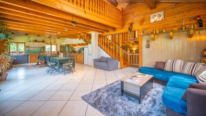 Amplia sala de estar con techo de madera, una escalera, zona de comedor y cocina.