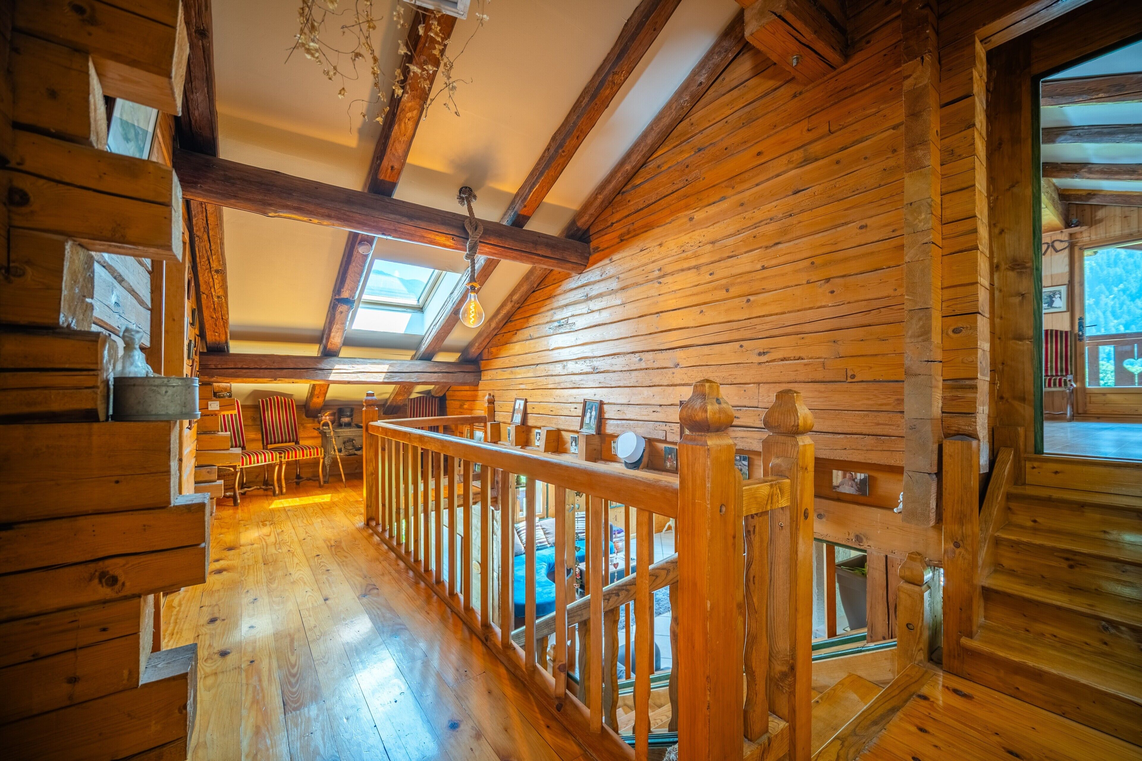 L’intérieur d’un chalet en bois, avec un escalier en bois, un balcon et une vue sur l’extérieur.