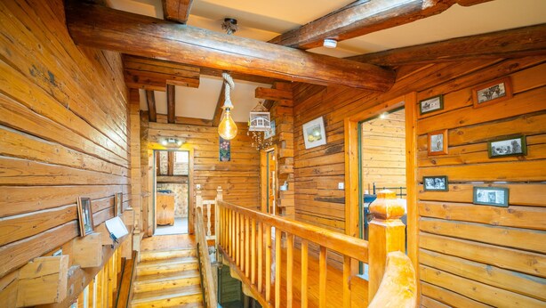Un interior de madera con una escalera, barandillas de madera y cuadros en las paredes.