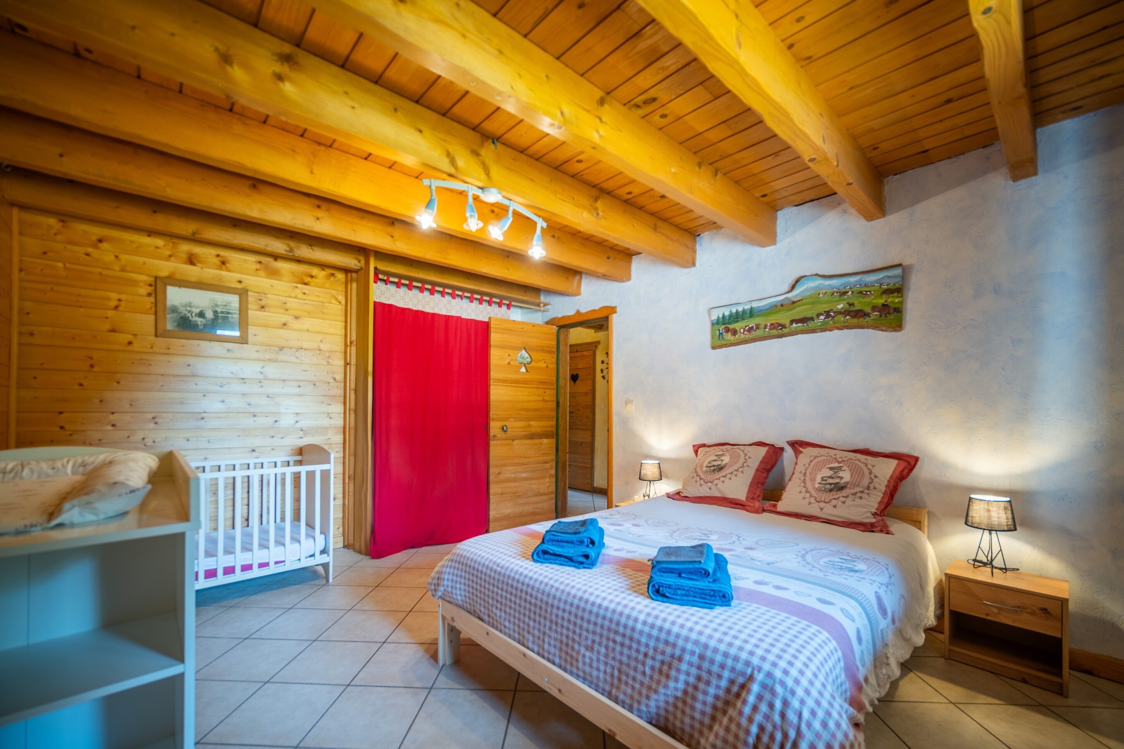 A wooden cabin bedroom with a bed, a crib, and a nightstand.