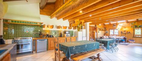 A spacious kitchen with wooden beams, a dining area with a table and chairs, and a living area with a sofa and a fireplace.