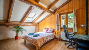 Una habitación con techo de madera, una cama con colcha a cuadros, un escritorio con silla y una planta en maceta.