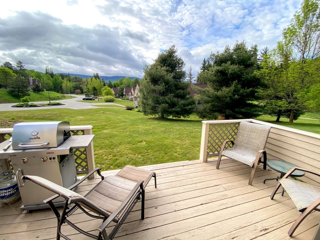 A deck with outdoor furniture and a grill, overlooking a green landscape with trees and a distant view of houses.