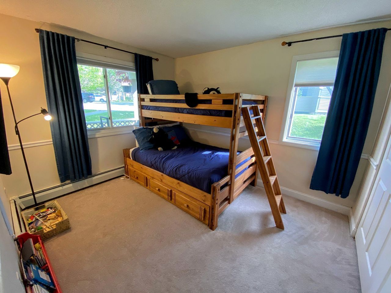A bunk bed with a ladder, a desk, and a lamp in a room with windows.