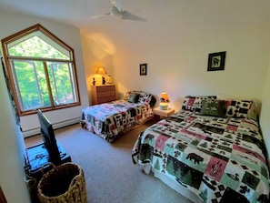 A bedroom with two beds, a desk, a chair, a television, and a window with a view of trees. - Ski Cabin Rental Ideal for a Mount Washington Vacation (Carroll)