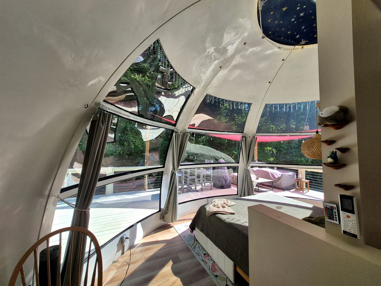 A room with a curved ceiling, a bed, a window, and a view of an outdoor area with a red umbrella.