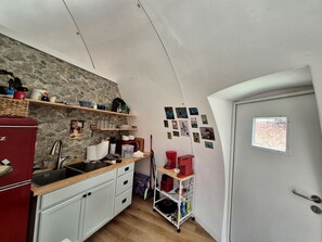 Eine kleine Küche mit einer Steinwand, einem roten Kühlschrank, einer Spüle und einem kleinen Fenster.