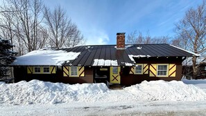 A two-story house with a metal roof and brick chimney, surrounded by snow and leafless trees. - Spacious Retreat for a White Mountains Vacation Getaway (Franconia)