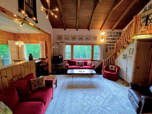 A cozy living room with a wooden ceiling, a red sofa, a coffee table, and a staircase leading to another level. - Spacious Retreat for a White Mountains Vacation Getaway (Franconia)