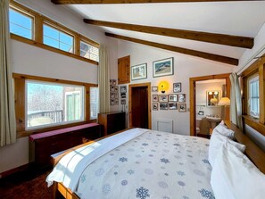 Ein Schlafzimmer mit Bett, Schreibtisch, Fenster und einem Badezimmer mit Spiegel und Waschbecken.
