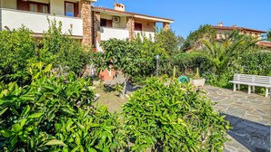 Ein Wohngebäude mit einer Steinfassade, mehreren Balkonen und einem Garten mit verschiedenen Pflanzen und einer Bank.